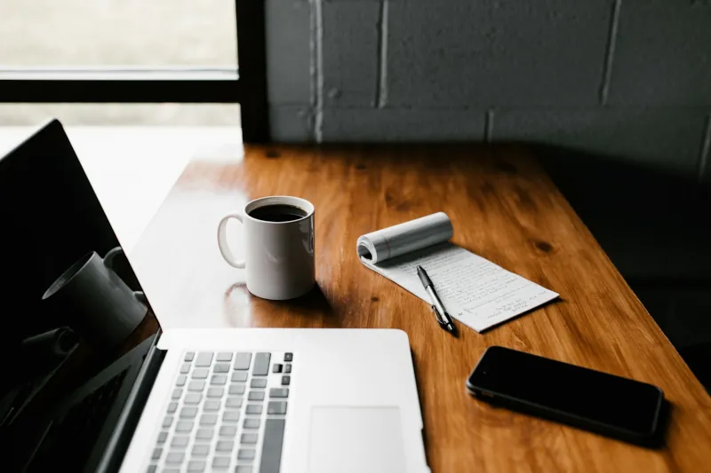 Laptop, phone, and handwritten plans on a working desk
